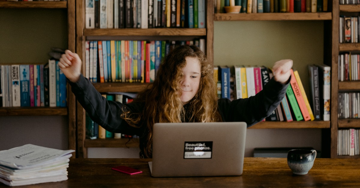 young girl at computer raising arms in acheivement
